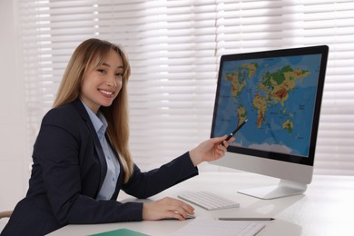 Happy manager showing world map on computer at desk in travel agency