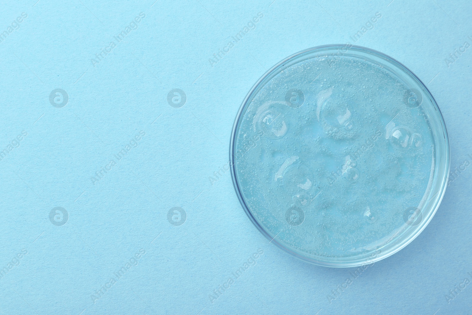 Photo of Petri dish with color liquid sample on light blue background, top view. Space for text
