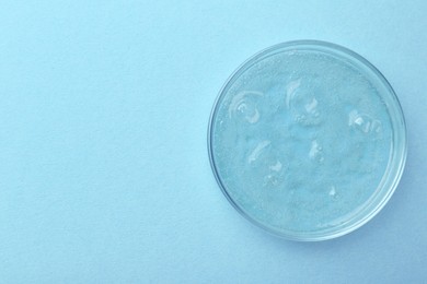 Petri dish with color liquid sample on light blue background, top view. Space for text