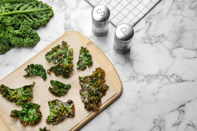 Tasty baked kale chips on marble table, flat lay