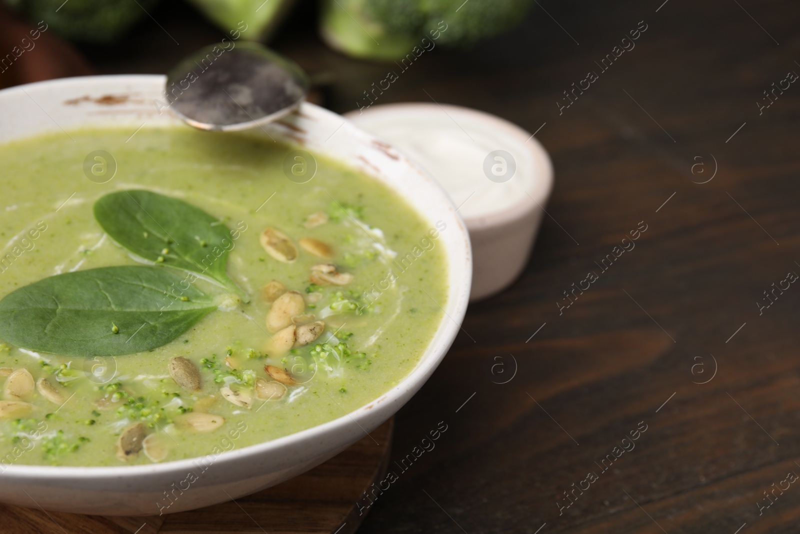 Photo of Delicious broccoli cream soup with basil and pumpkin seeds served on wooden table, closeup. Space for text