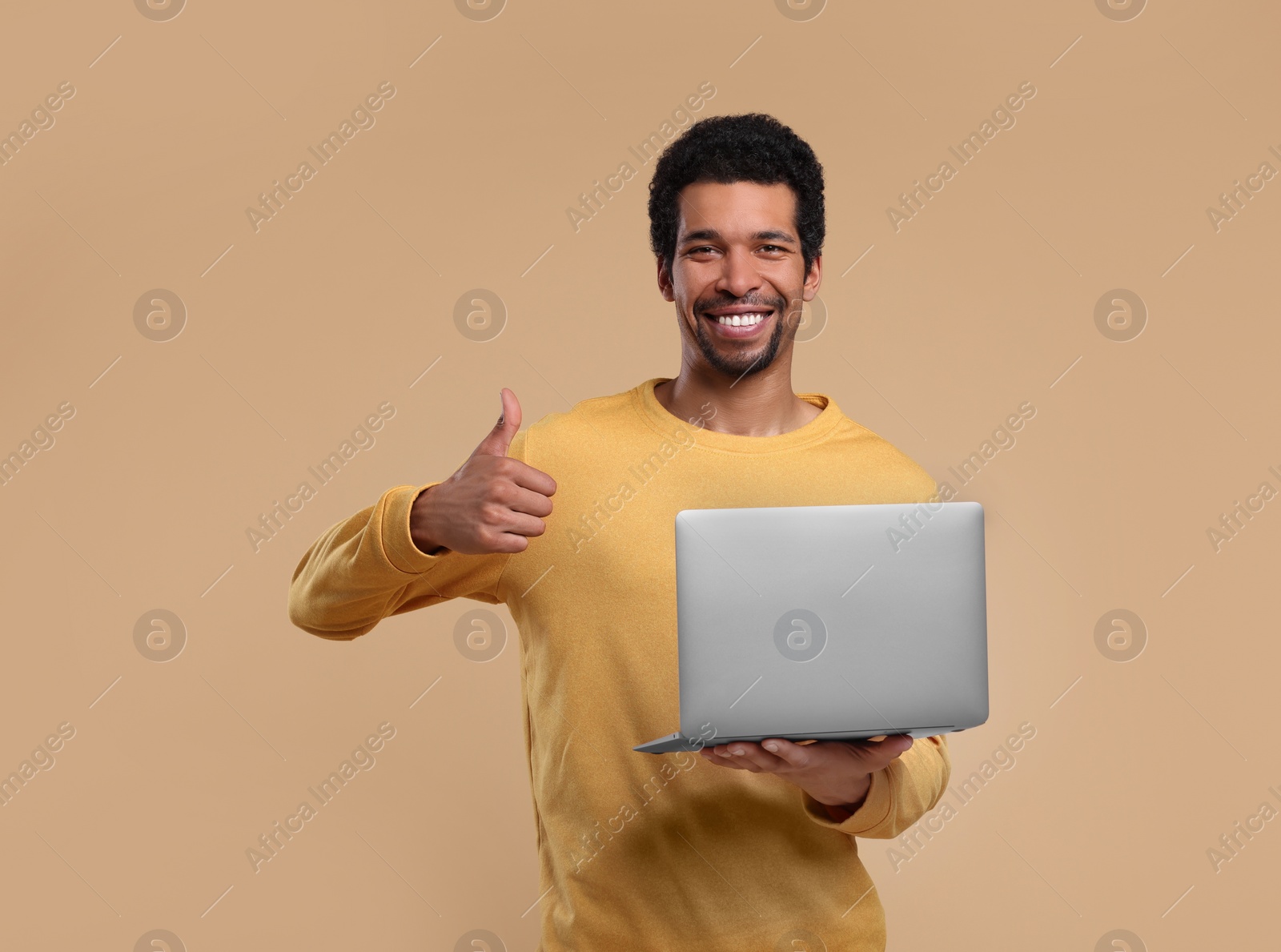 Photo of Happy man with laptop showing thumb up on beige background