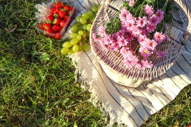 Photo of Picnic basket, flowers and berries on blanket outdoors