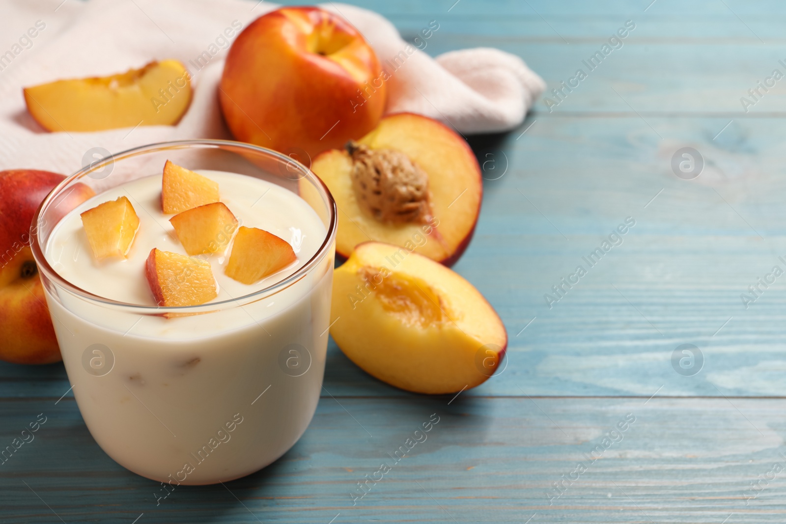Photo of Tasty peach yogurt with pieces of fruit in glass on light blue wooden table, space for text