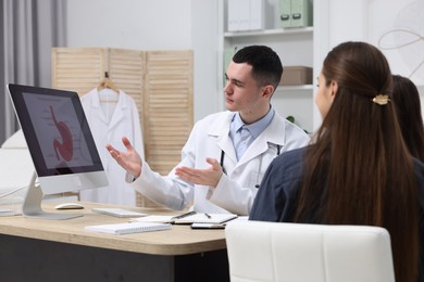 Gastroenterologist consulting woman with her daughter and showing image of stomach on computer in clinic