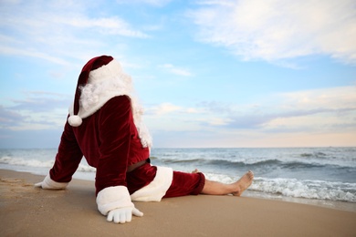 Photo of Santa Claus relaxing on beach, space for text. Christmas vacation