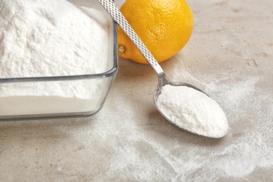 Photo of Bowl and spoon of baking soda with lemon on gray table, closeup