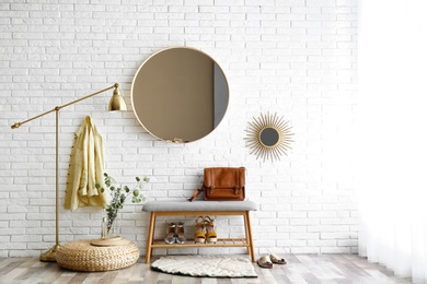 Photo of Hallway interior with big round mirror and shoe storage bench near brick wall