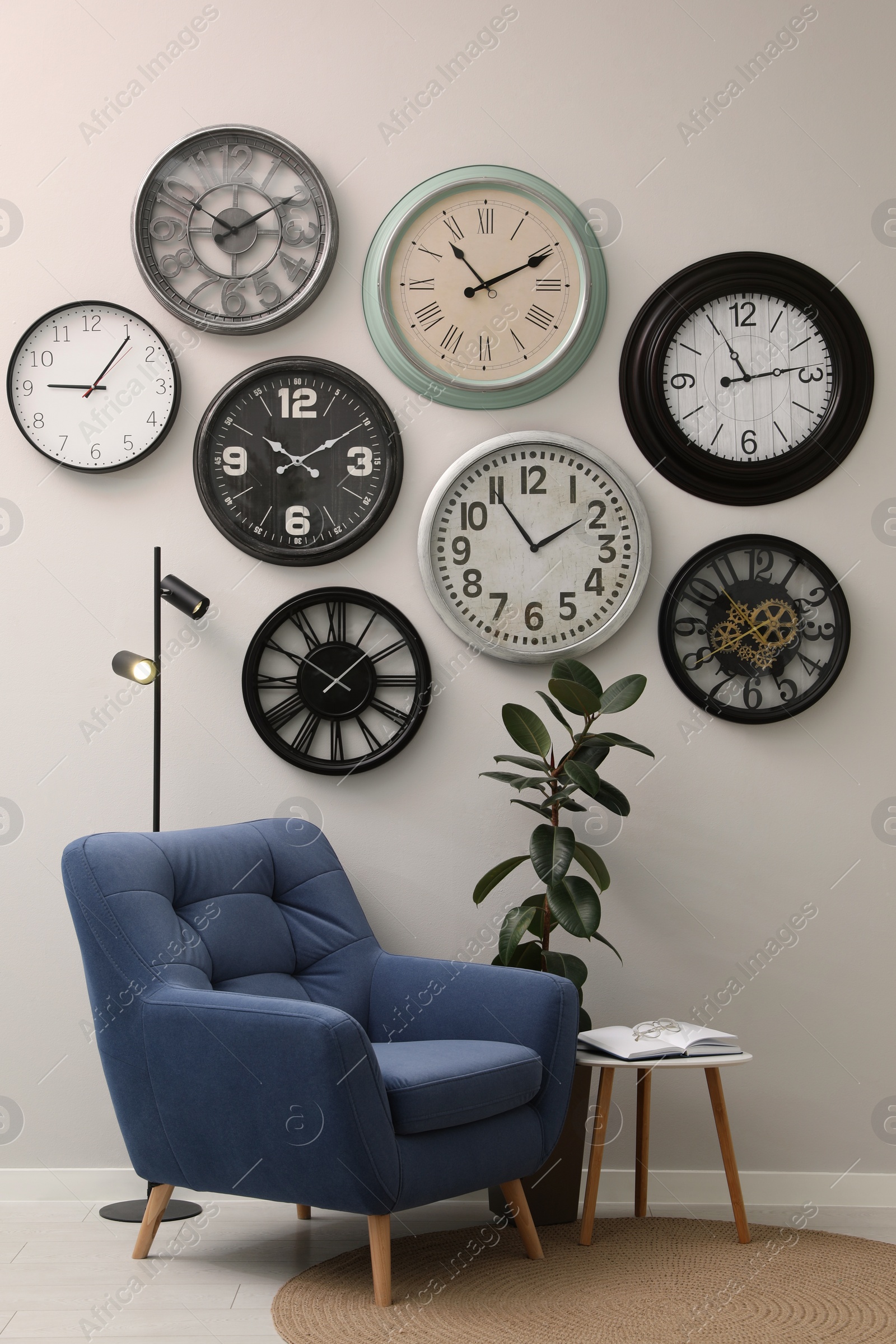 Photo of Armchair, table and many different clocks hanging on white wall in room