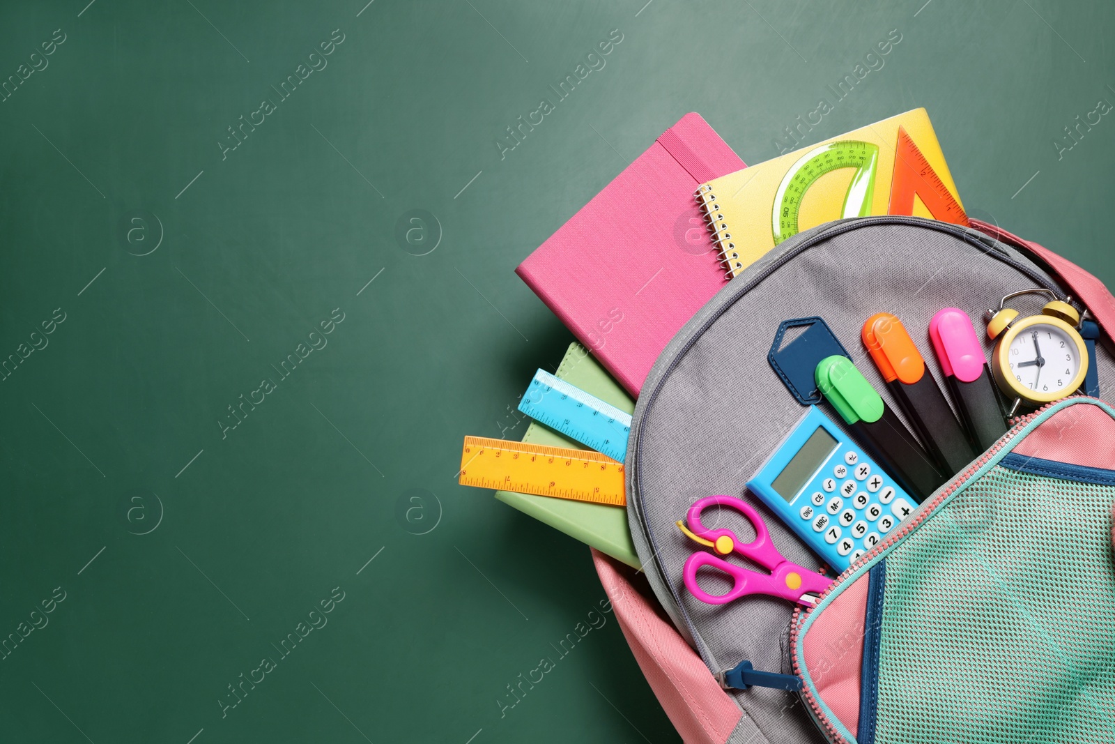 Photo of Backpack with different stationery on chalkboard background, top view. Space for text