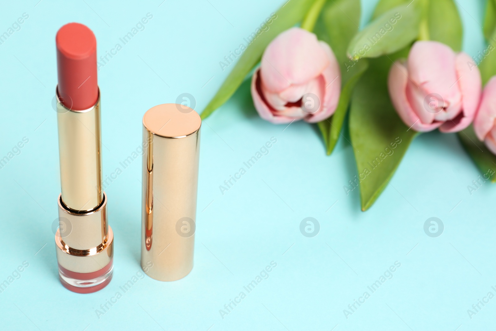 Photo of Bright lipstick and flowers on light blue background, space for text