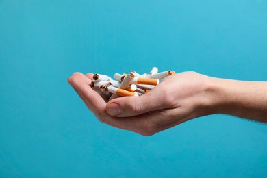 Photo of Stop smoking. Man holding broken cigarettes on light blue background, closeup