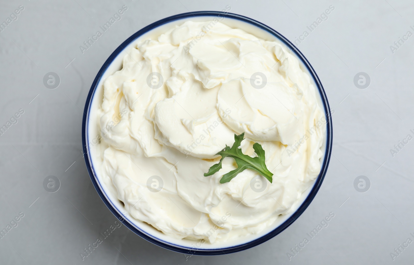 Photo of Bowl of tasty cream cheese and arugula on grey table, top view