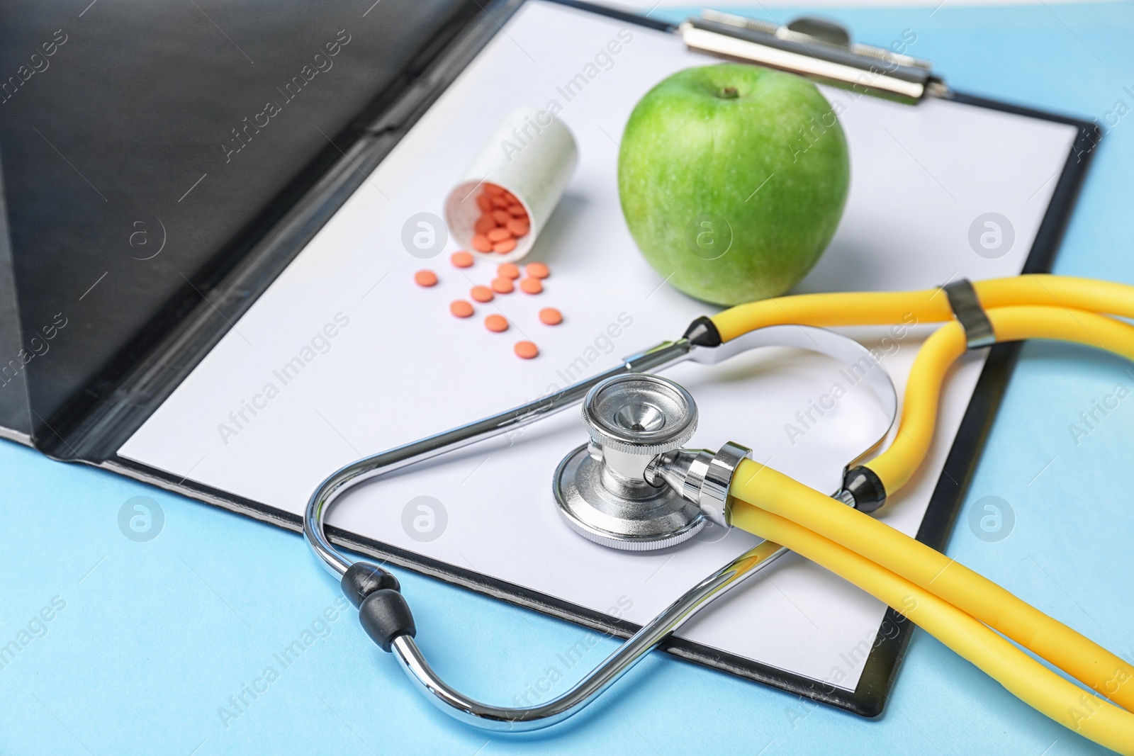 Photo of Composition with stethoscope, clipboard, pills and apple on color background. Medical equipment