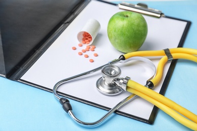 Composition with stethoscope, clipboard, pills and apple on color background. Medical equipment