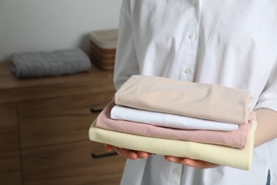 Woman holding folded clothes at home, closeup. Space for text