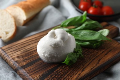 Photo of Delicious burrata cheese with basil on light grey tablecloth, closeup