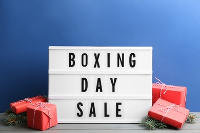 Composition with Boxing Day Sale sign and Christmas gifts on white table against blue background