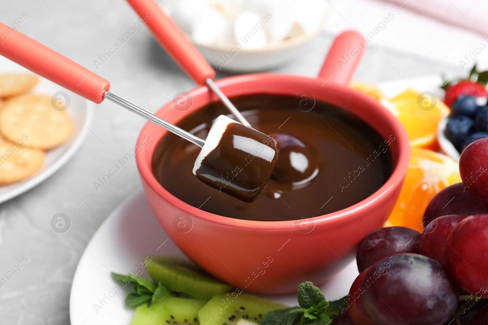 Photo of Dipping marshmallow into pot with chocolate fondue on table