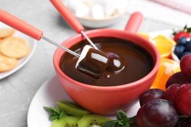 Photo of Dipping marshmallow into pot with chocolate fondue on table