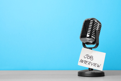 Photo of Retro microphone and reminder note with words JOB INTERVIEW on wooden table against light blue background, space for text