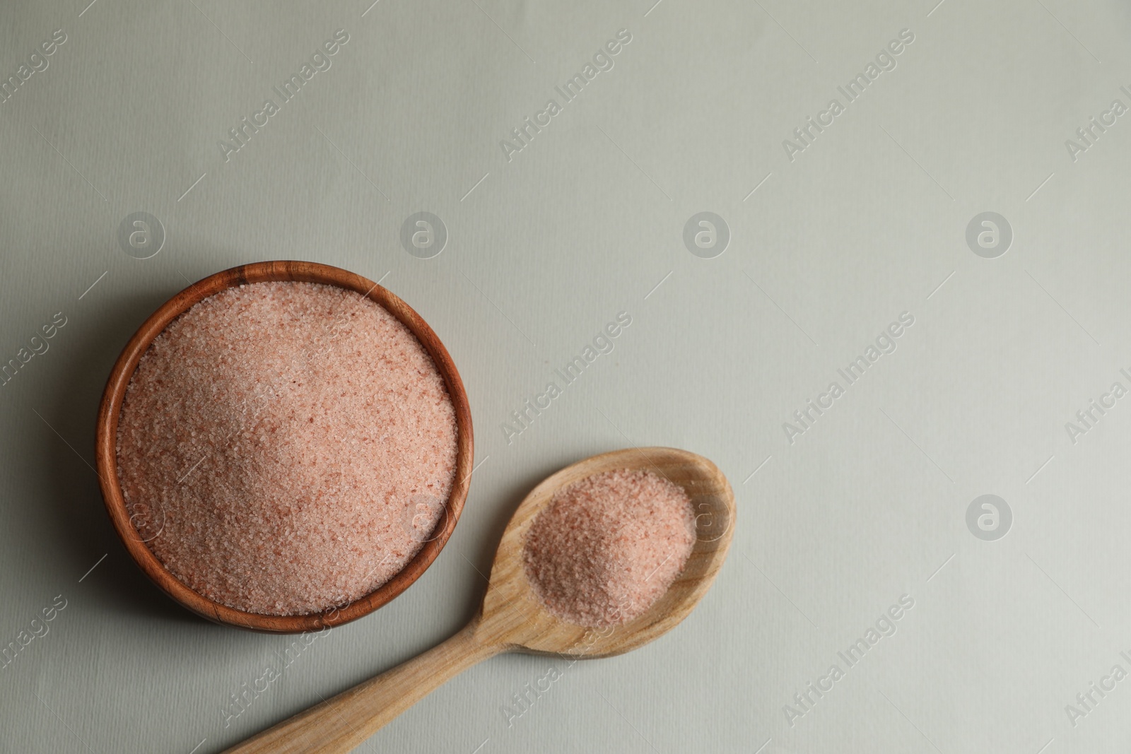 Photo of Himalayan salt in bowl and spoon on grey background, flat lay. Space for text