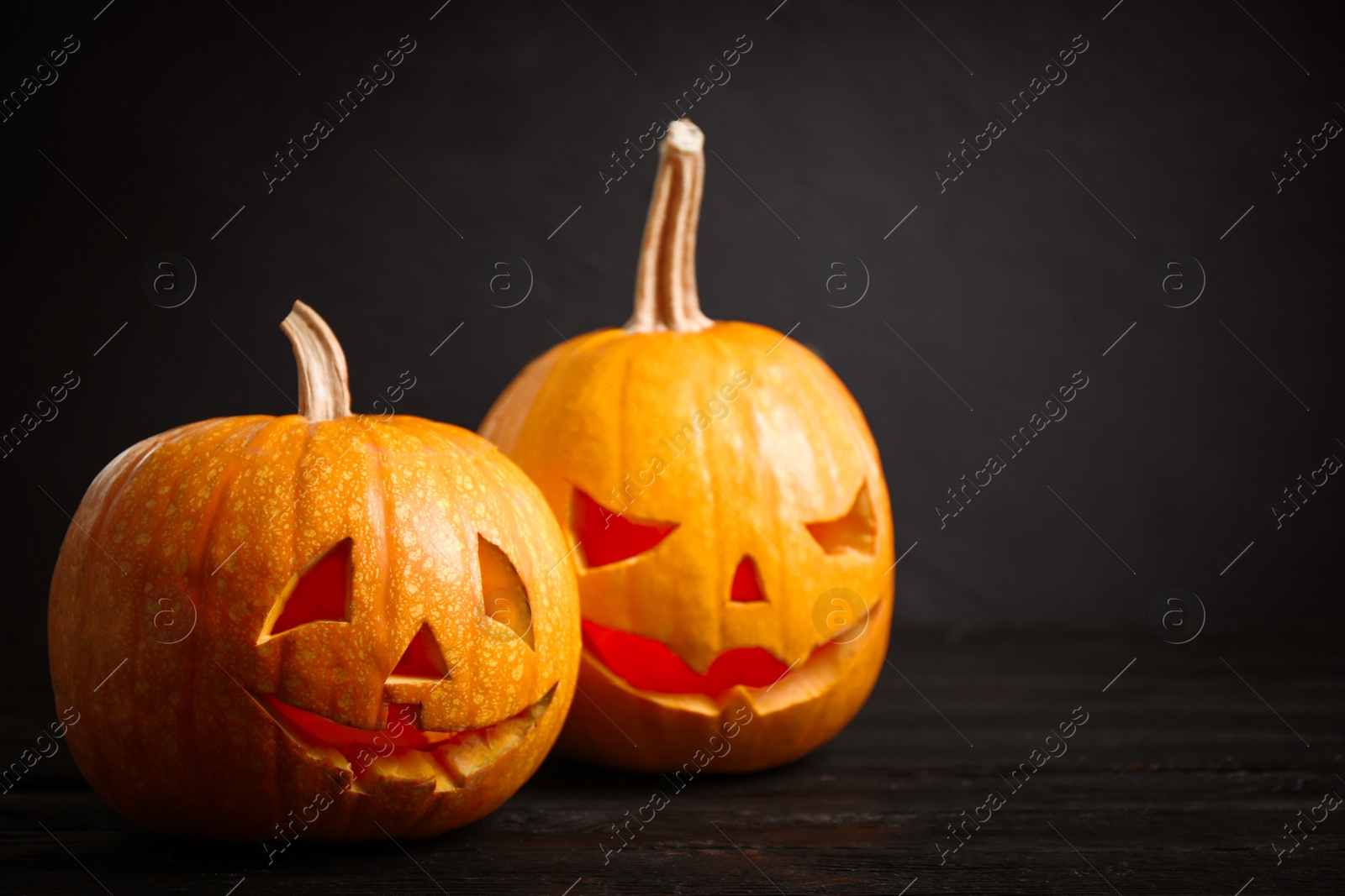 Photo of Spooky Jack pumpkin head lanterns on wooden table against black background. Halloween decoration