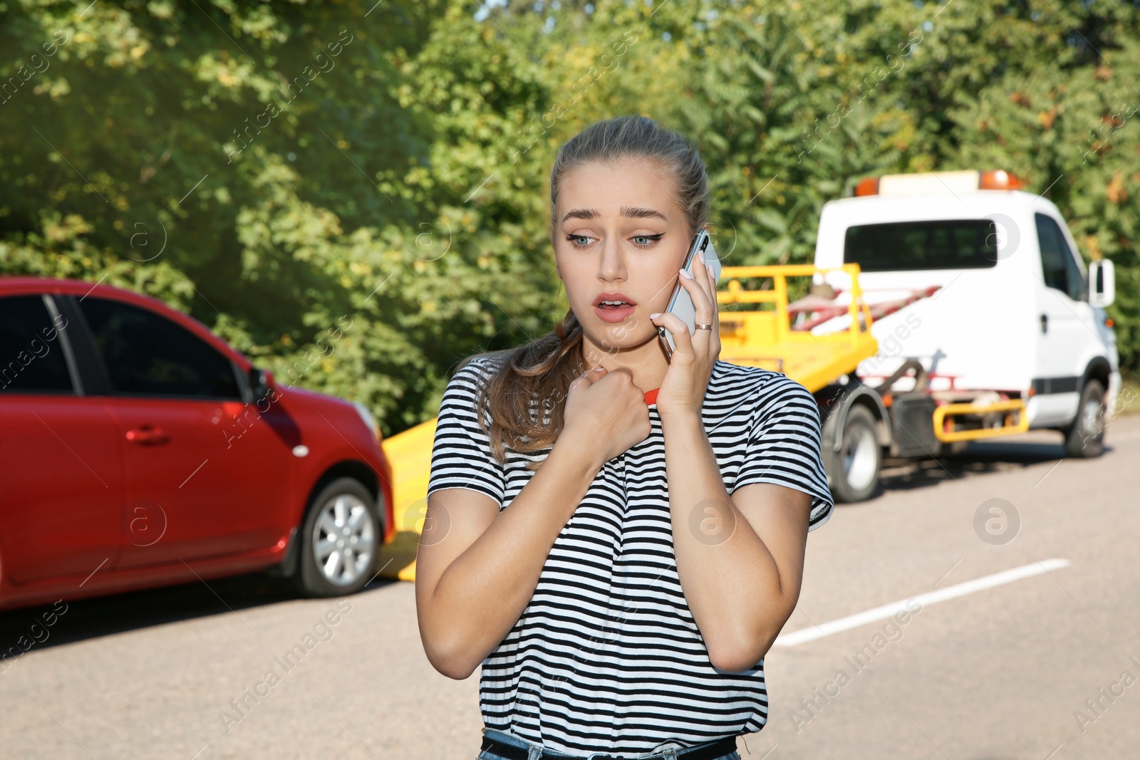 Photo of Woman talking on phone near broken car and tow truck outdoors