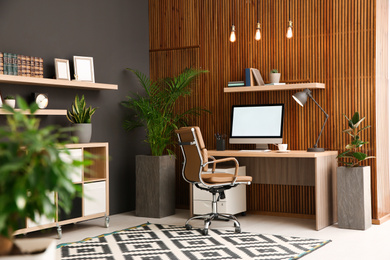 Photo of Comfortable workplace with computer near wooden wall in stylish room interior. Home office design