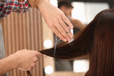 Barber making stylish haircut with professional scissors in beauty salon, closeup