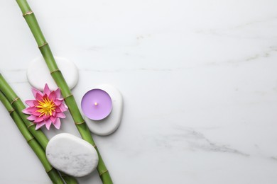 Photo of Bamboo stems, flower, spa stones and burning candle on white marble table, flat lay. Space for text