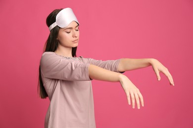 Photo of Young woman wearing pajamas and mask in sleepwalking state on pink background