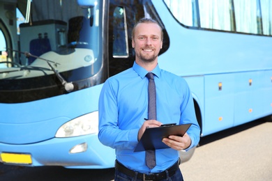 Professional driver with clipboard near bus. Passenger transportation