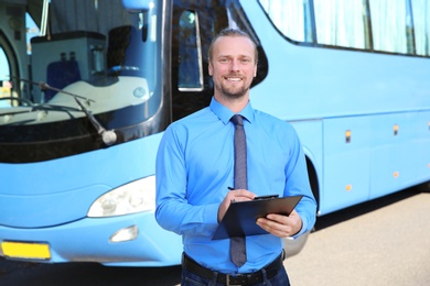 Photo of Professional driver with clipboard near bus. Passenger transportation