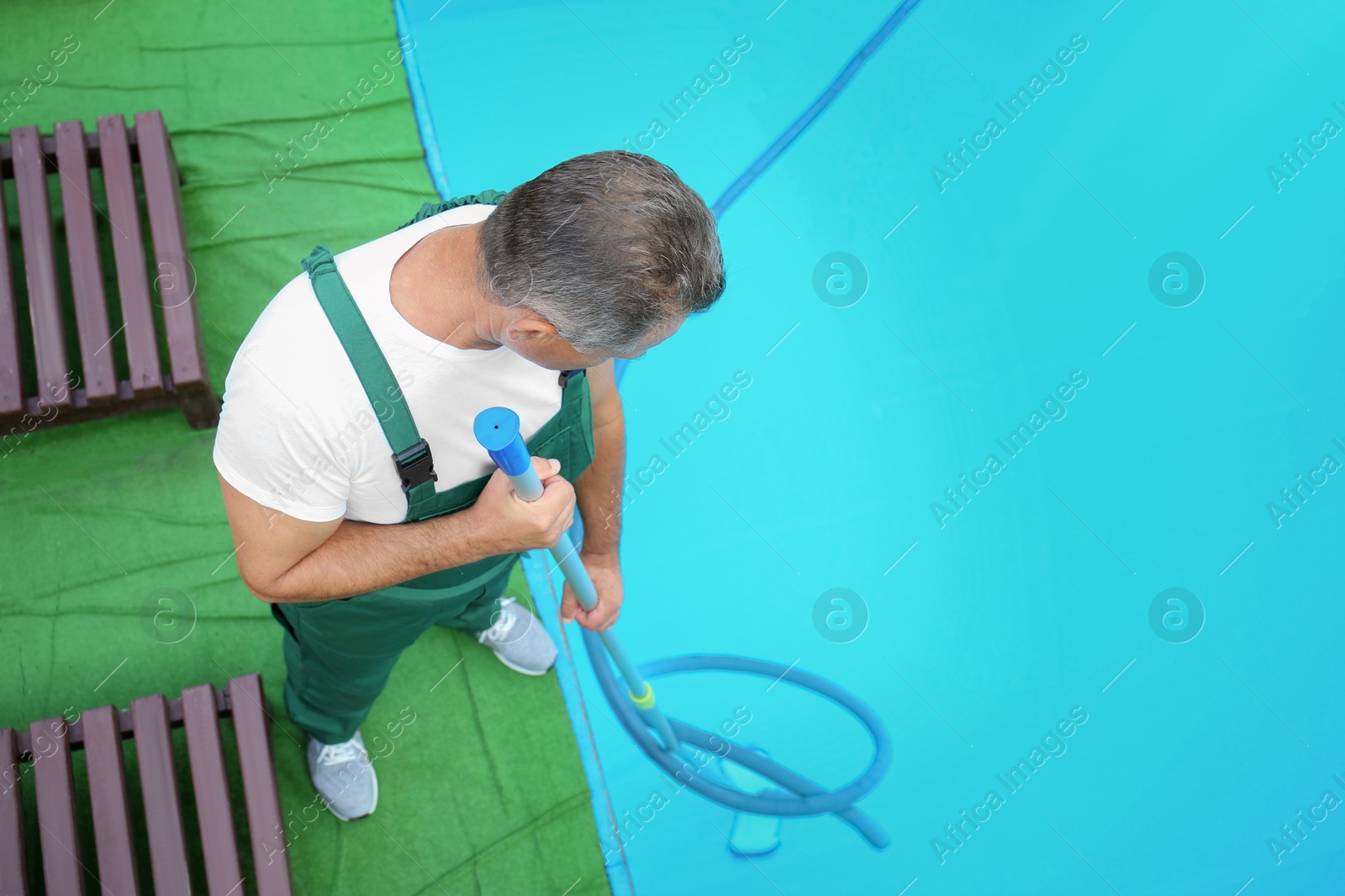 Photo of Male worker cleaning outdoor pool with underwater vacuum, above view