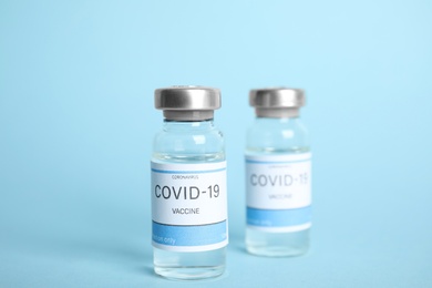 Vials with coronavirus vaccine on light blue background