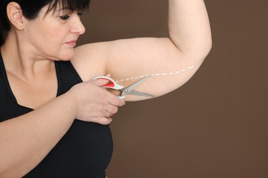 Photo of Obese woman with scissors on brown background, space for text. Weight loss surgery