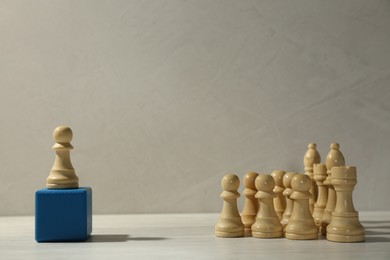 White chess piece standing out from others on wooden table against grey background