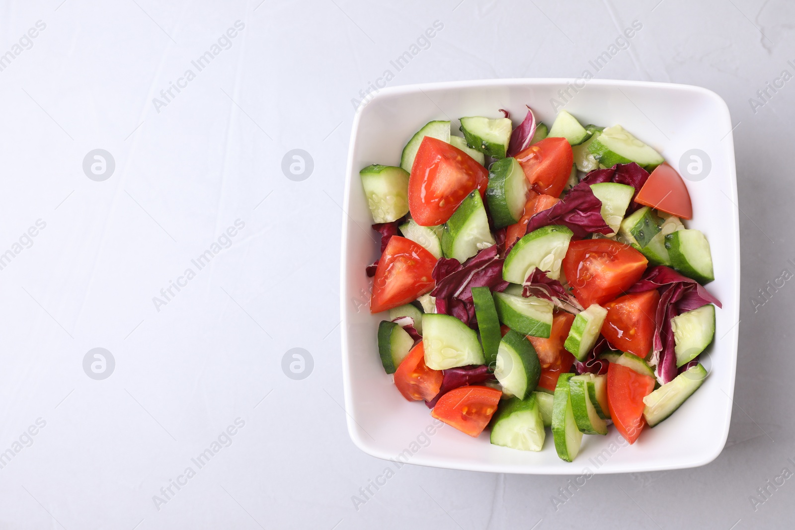 Photo of Bowl of vegetarian salad with cucumber, tomato, cabbage and onion on light background, top view. Space for text