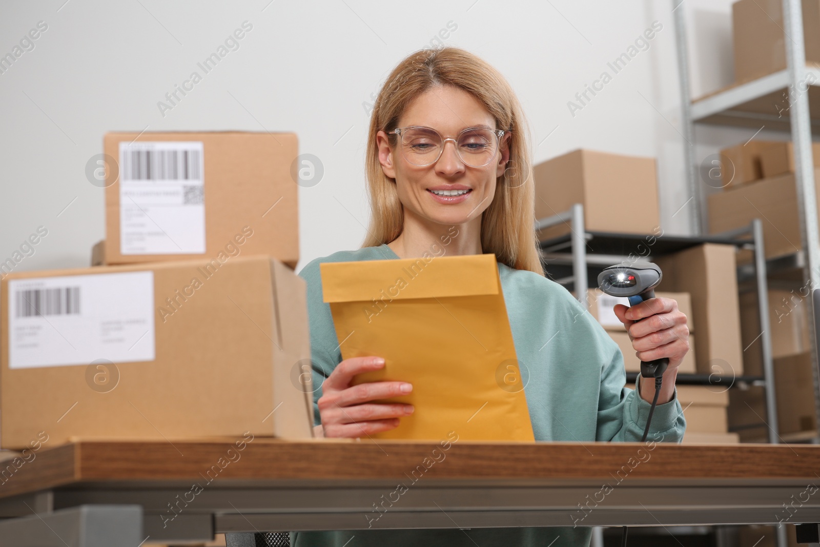 Photo of Seller with scanner reading parcel barcode at table in office. Online store