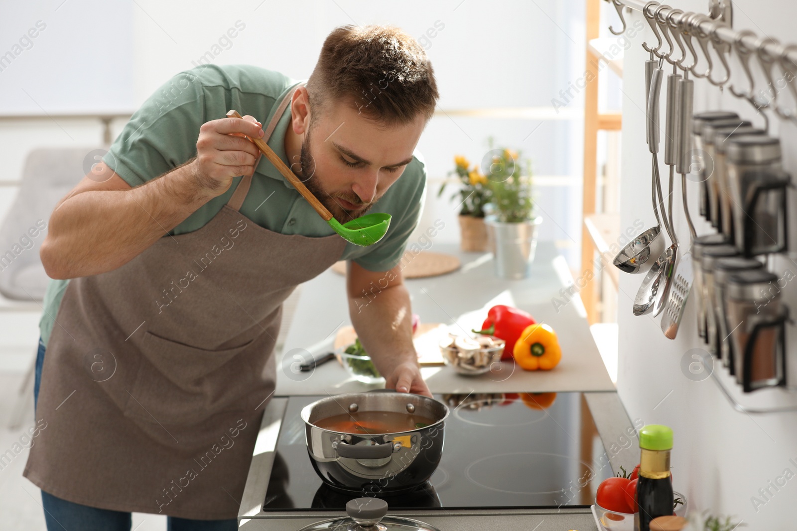 Photo of Young man cooking delicious soup in kitchen