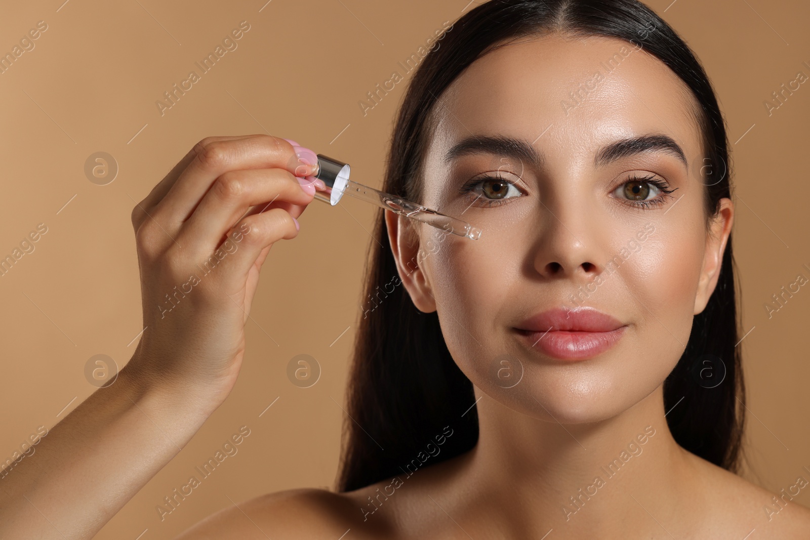 Photo of Beautiful young woman applying serum onto her face on beige background, closeup