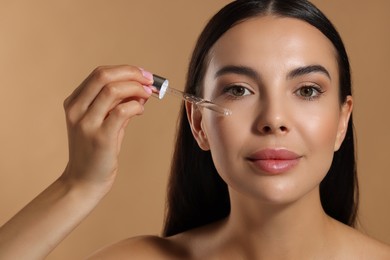 Beautiful young woman applying serum onto her face on beige background, closeup