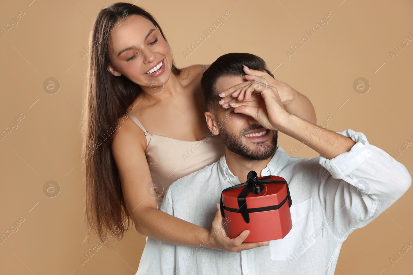 Photo of Woman presenting gift to her boyfriend on beige background