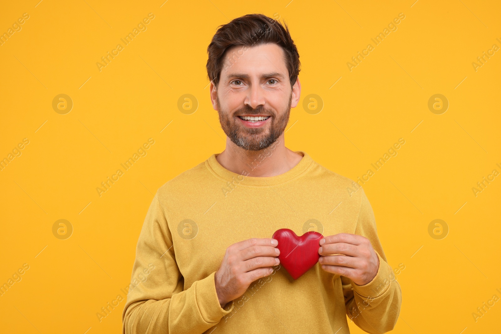 Photo of Happy man holding red heart on orange background