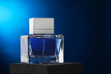 Photo of Luxury men`s perfume in bottle against dark blue background, space for text