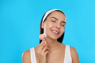 Photo of Young woman using facial cleansing brush on light blue background. Washing accessory