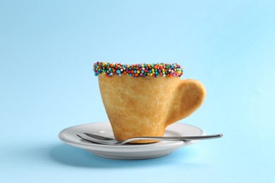 Photo of Delicious edible biscuit coffee cup decorated with sprinkles and spoon on light blue background