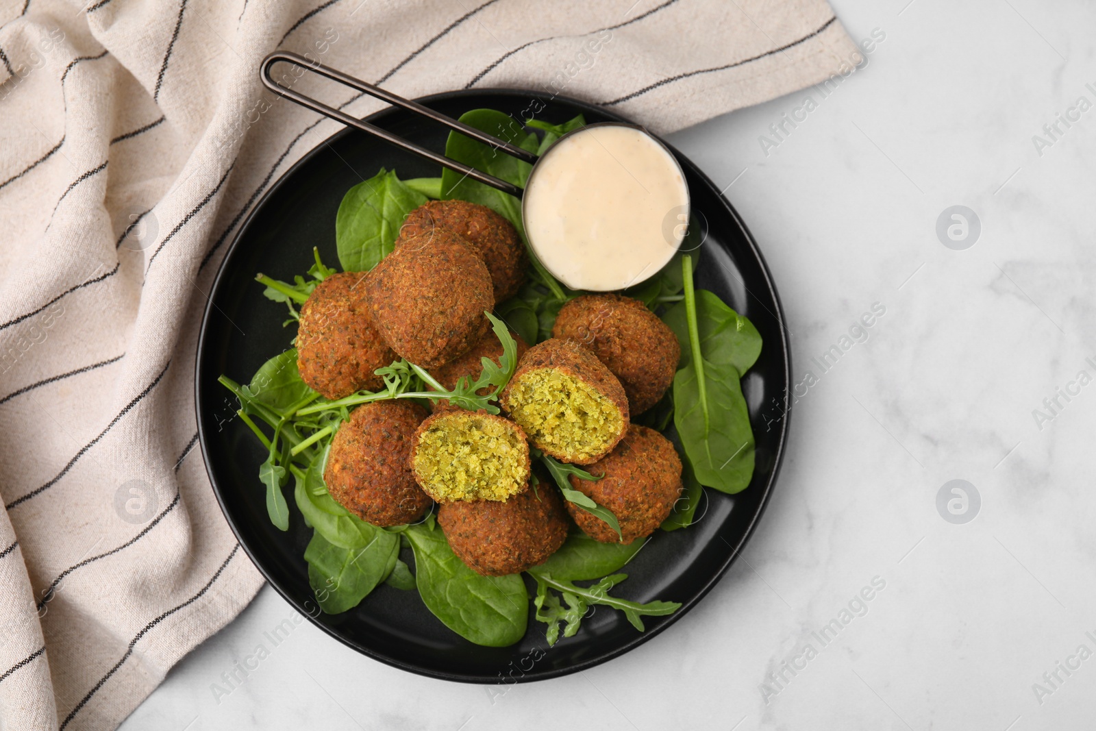 Photo of Delicious falafel balls, herbs and sauce on white marble table, top view