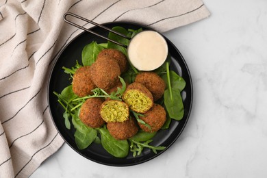 Photo of Delicious falafel balls, herbs and sauce on white marble table, top view